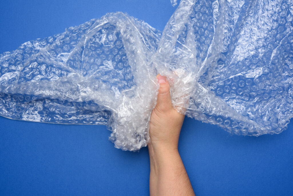 female hand holding crumpled piece of polyethylene with air bubbles on a blue background, packing material