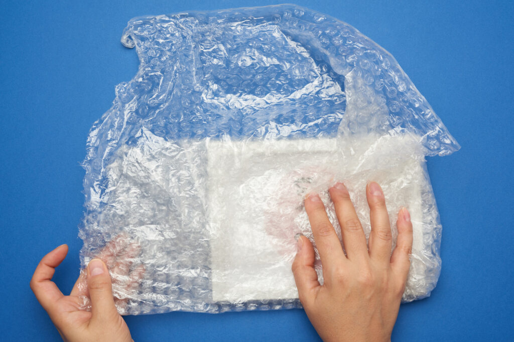 two female hands are wrapping the item in a transparent plastic wrap with bubbles, blue background