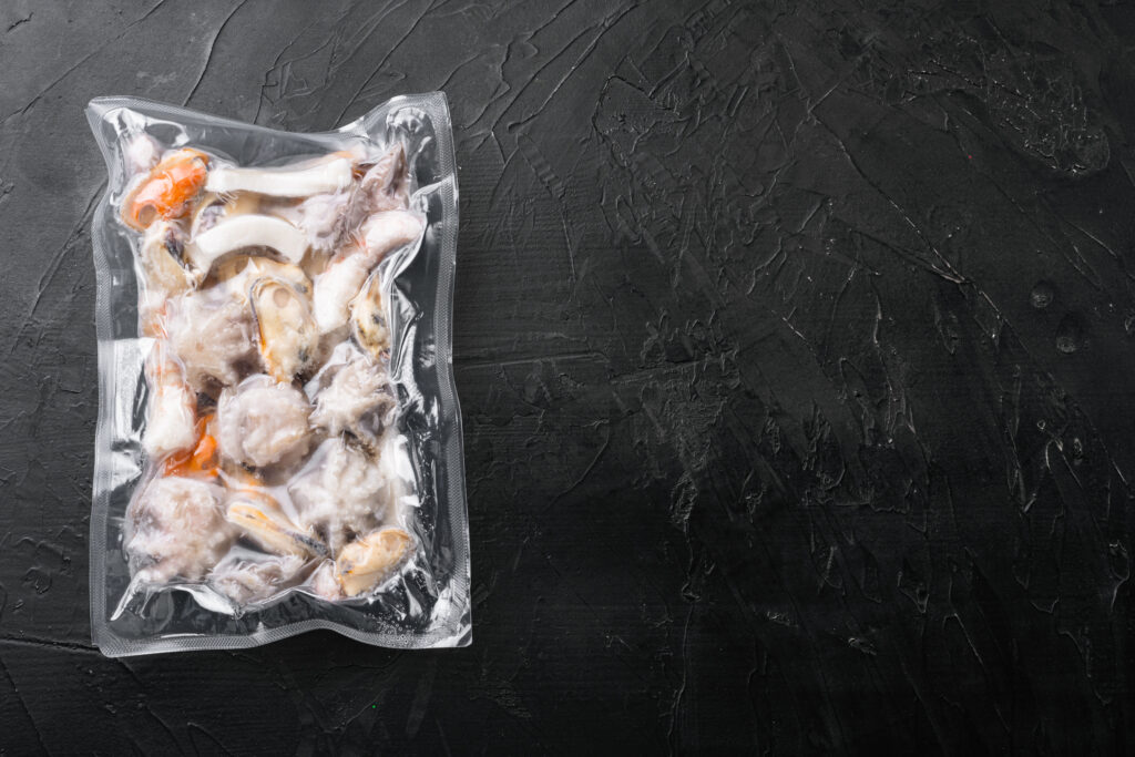 Raw seafood, mussels, squid octopus in vacuum pack set, on black dark stone table background, top view flat lay, with copy space for text
